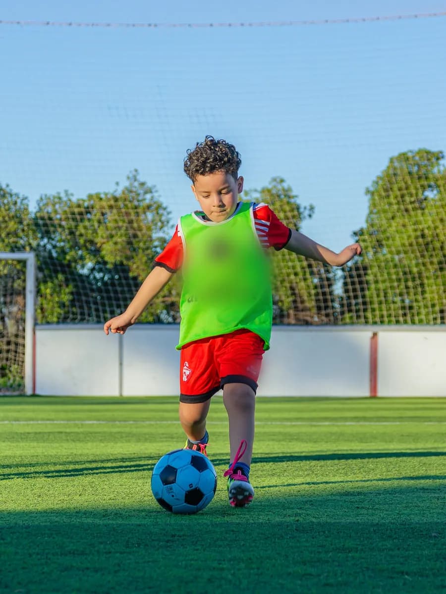 Jeune joueur d'académie en chasuble et tenue rouge conduisant le ballon