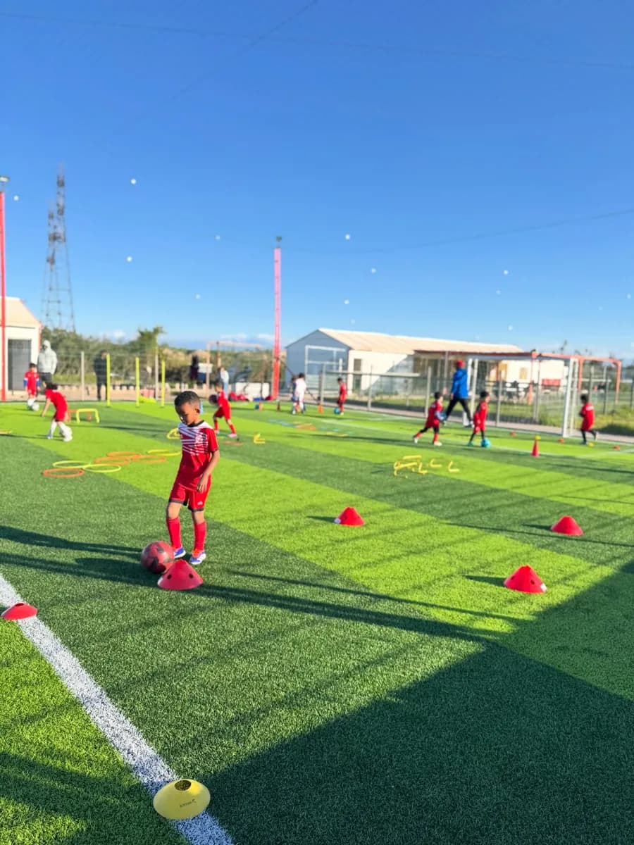 Séance d'entraînement d'une académie de football : jeunes joueurs en tenue rouge, plots et cerceaux sur un terrain synthétique
