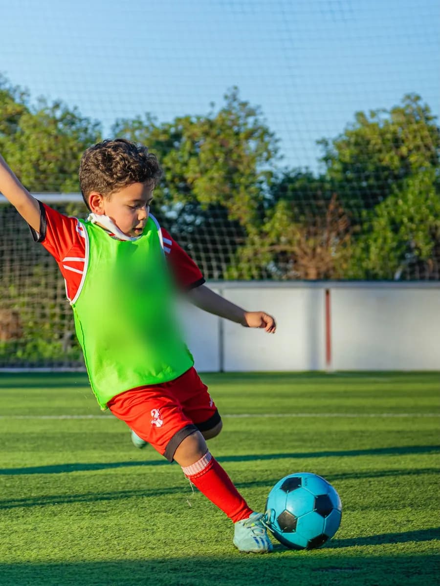 Jeune joueur d'académie en chasuble frappant le ballon à l'entraînement